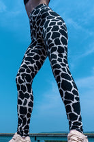 Woman wearing cotton lycra leggings in the cream black cow print shown from the front with a blue sky in the background