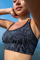 model wearing a greyblack feather cross-back bra from funky simplicity shown from the front with a blue sky and ocean on the background
