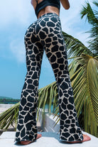 Woman wearing cotton lycra Flares in Cream Black Dutch Cow print from Funky Simplicity shown from the back with  leaves of a palmtree in the background with a cloudy blue sky