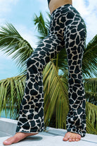 Woman wearing cotton lycra Flares in Cream Black Dutch Cow print from Funky Simplicity shown from the front with  leaves of a palmtree in the background with a cloudy blue sky