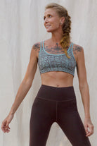 Woman wearing an Argus patterned sports bra and brown leggings against a plain background