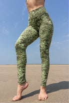 Model wearing green Bloom printed leggings standing on a beach with a clear blue sky.