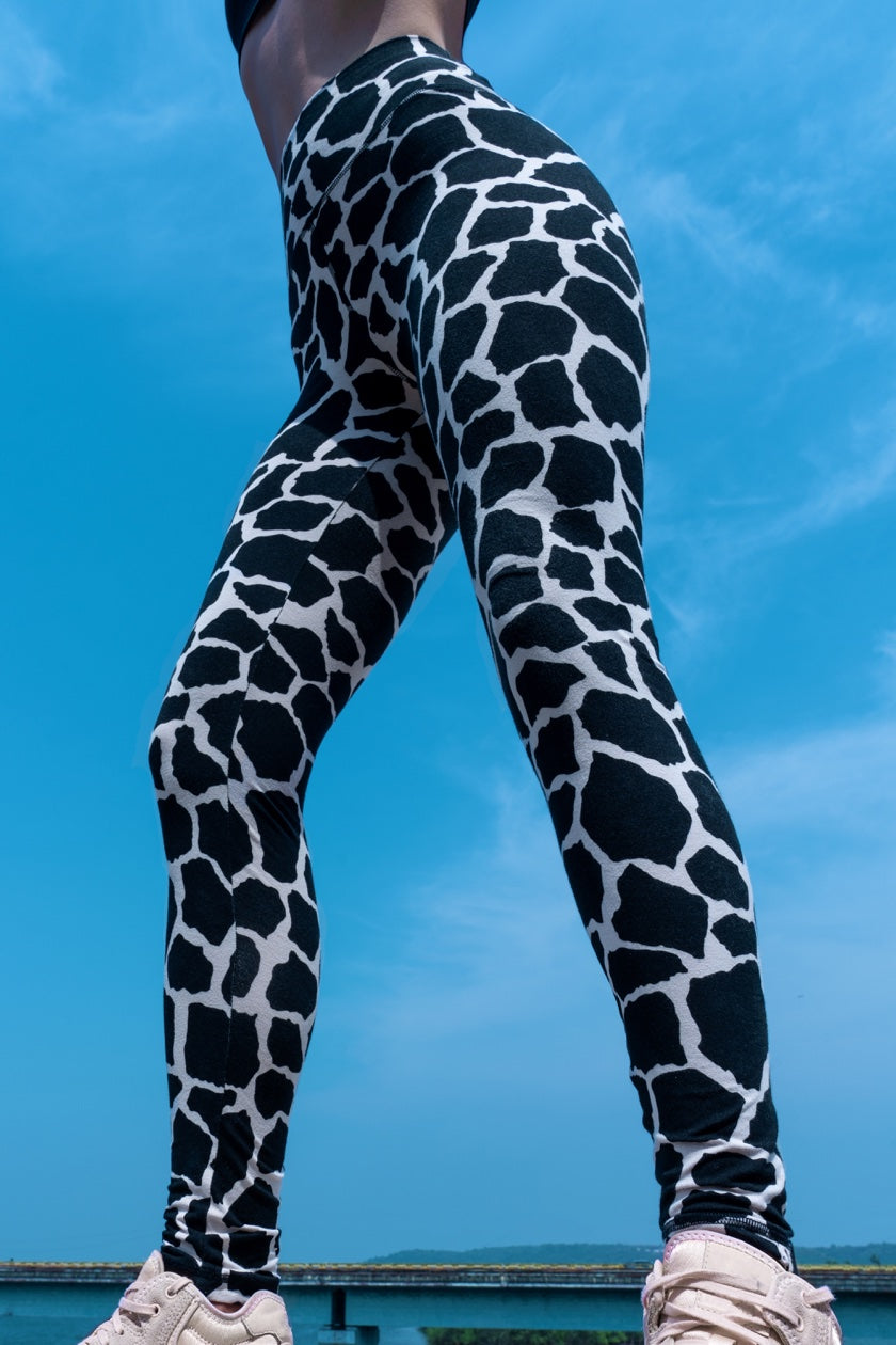 Woman wearing cotton lycra leggings in the cream black cow print shown from the front with a blue sky in the background