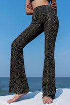 Woman wearing olive black Snake patterned  flared leggings from Funky Simplicity - standing on a white surface with a blue sky and ocean background